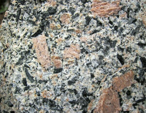 A close up view of porphyritic granite, a type of igneous rock. Porphyritic granite occurs when the temperature of the magma cooling changes quickly. In this instance, large crystals were allowed to form with slow cooling, only to be interrupted by a sudden decreasing temperature change that sped up the crystallization process, resulting in smaller crystals.